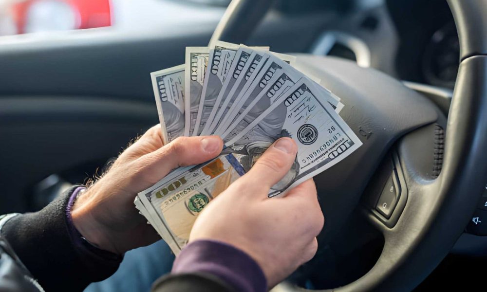 Venice cash for cars—driver holding fan of $100 bills inside vehicle.