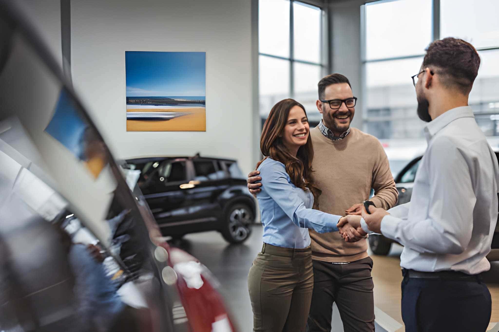 Auto dealers Bradenton FL—couple shakes hands with salesperson inside modern car dealership showroom.