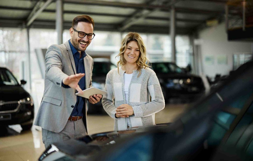 Car dealers near me—salesman with tablet showing vehicle features to smiling customer in showroom.