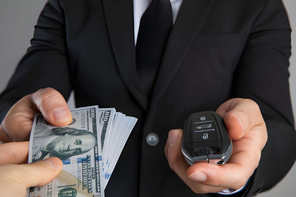 Cash for cars near me—man in suit handing car key fob while receiving stack of hundred-dollar bills.