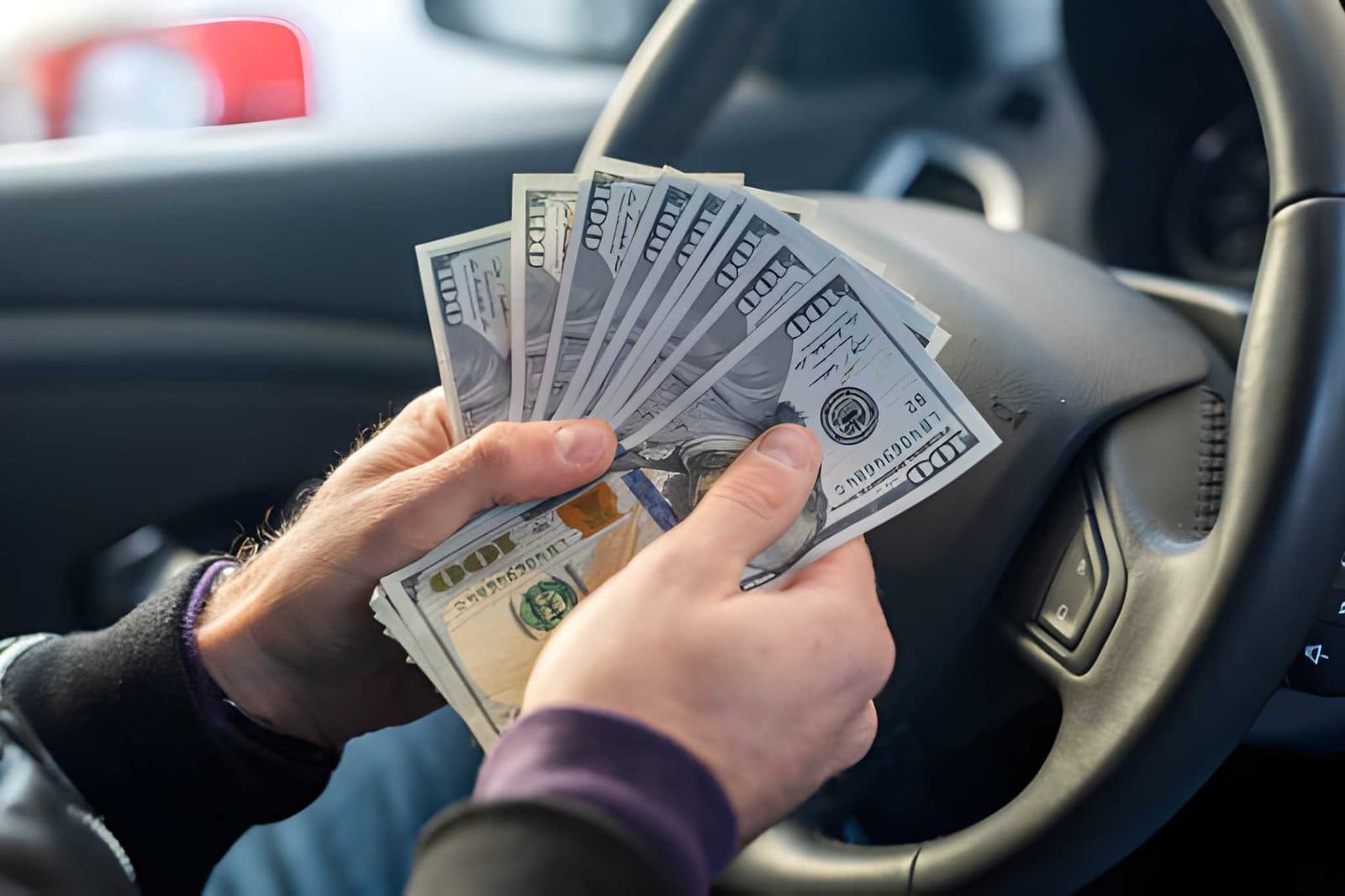 Venice cash for cars—driver holding fan of $100 bills inside vehicle.