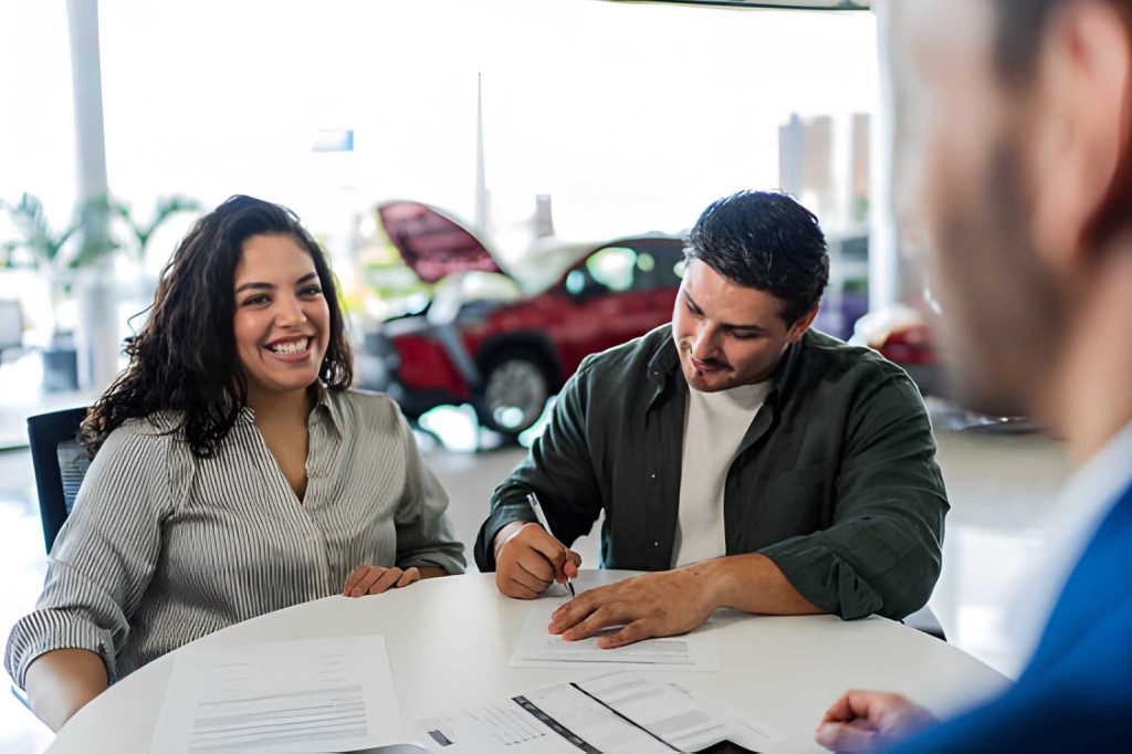 Buy here pay here cars near me—customer signing paperwork at dealership with red car in background.