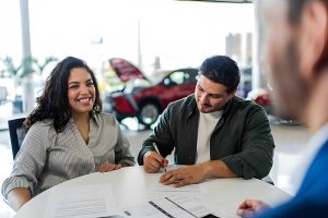 Buy here pay here cars near me—customer signing paperwork at dealership with red car in background.