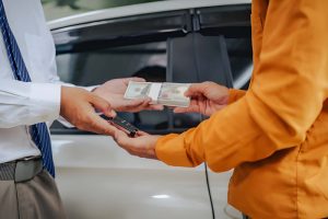 Buy here pay here Sarasota FL—customer exchanging cash for car keys in front of vehicle.