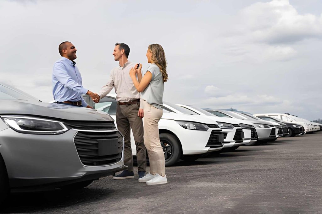 Used car dealers Bradenton customers shaking hands near silver car with keys during purchase agreement