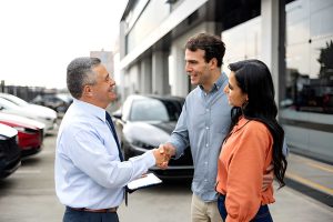Car dealers in Venice FL assisting customers with vehicle purchase and professional handshake outside dealership.