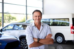 Bradenton auto dealers professional standing in showroom with cars on display and natural light from large windows.