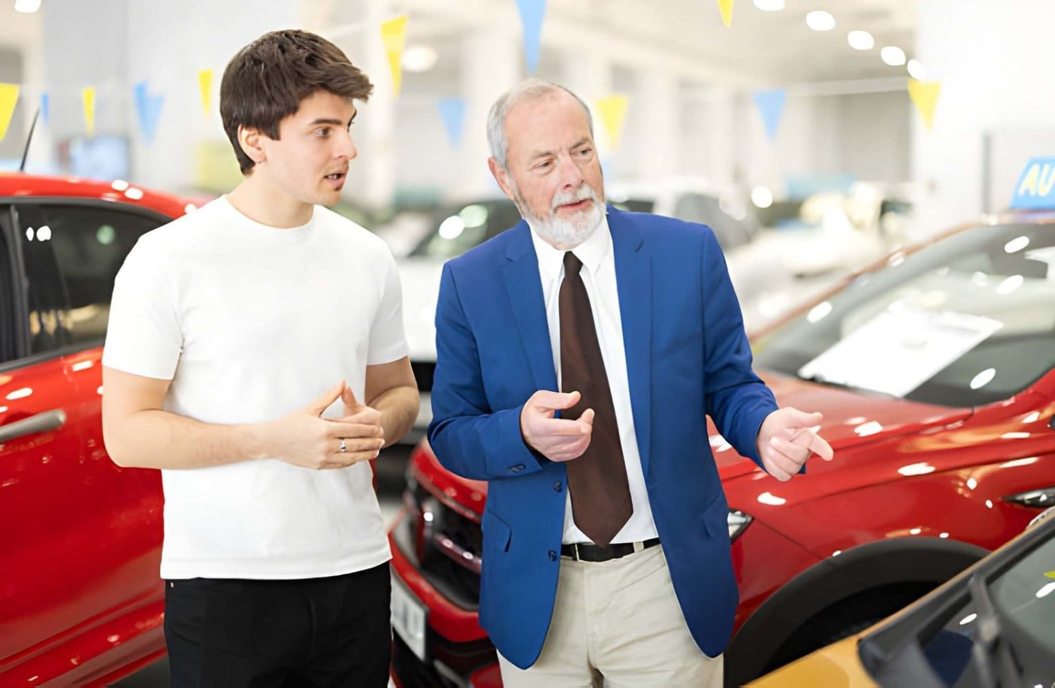 Used car dealers in Venice Florida consultant discussing vehicle options with customer near colorful cars in dealership.