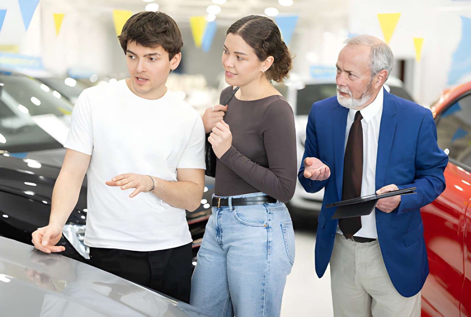 Used car dealers in Venice Florida salesperson with clipboard discussing vehicle features with young couple in dealership.