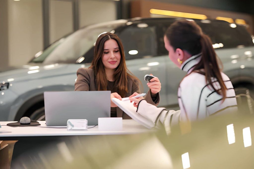 Auto Dealers Boca Raton Florida customer receiving car keys during purchase agreement at dealership desk.