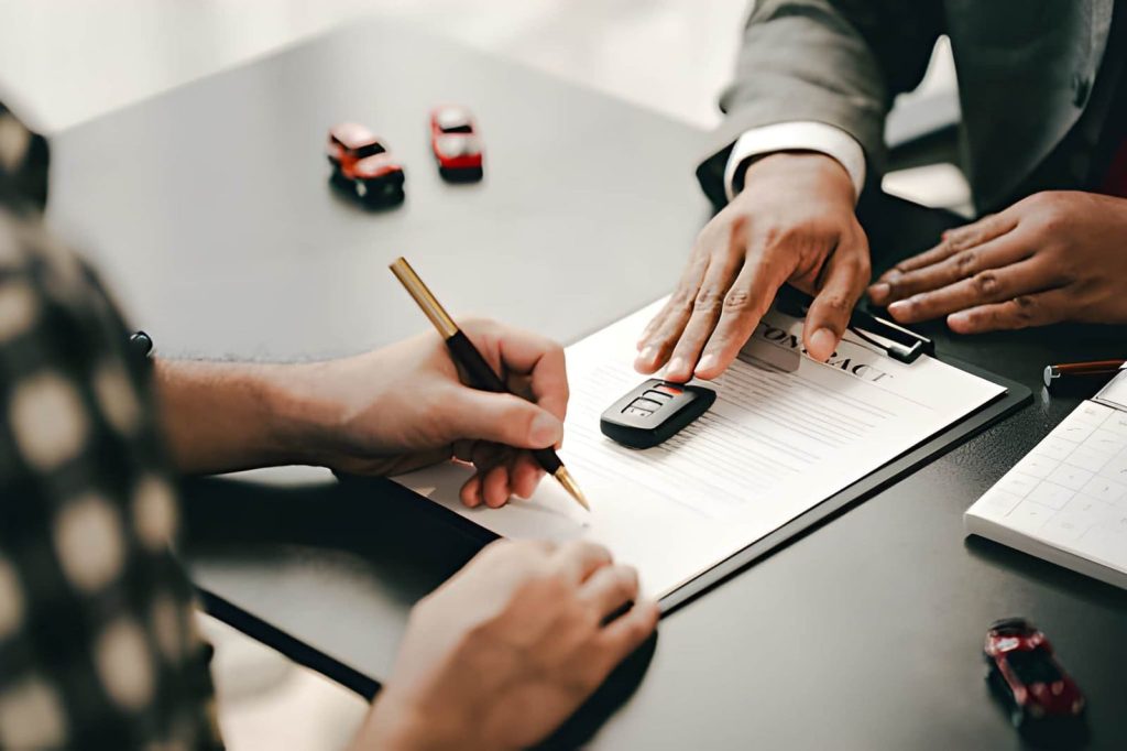 Buy here pay here Sarasota FL customer signing an auto financing agreement contract next to car keys and a sales representative.