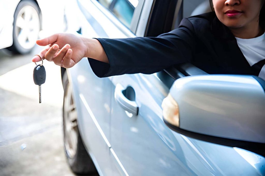 Car dealers in Boca Raton Florida driver leaning out of a blue sedan window handing over a car key.